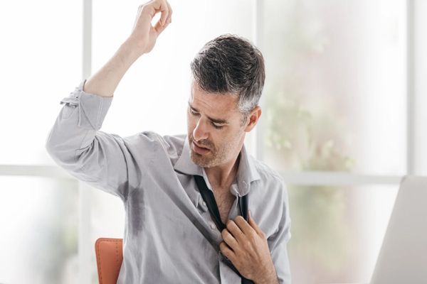 Hiperhidrosis - Hombre en el trabajo con camisa quitándose la corbata mientras mira la axila del brazo derecho con un exceso de sudoración