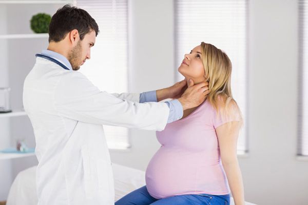Especialista en su consulta explorando la tiroides de mujer embarazada 