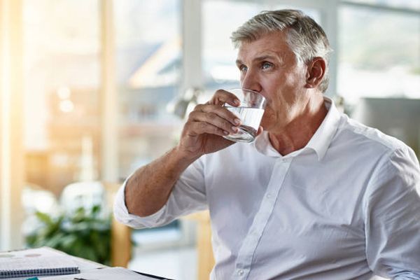 Hiperhidrosis - hombre mayor sentado en la oficina bebiéndose un vaso de agua
