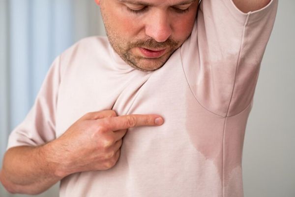 Hombre adulto señalándose la zona de la axila de su camiseta afectada por el exceso de sudor
