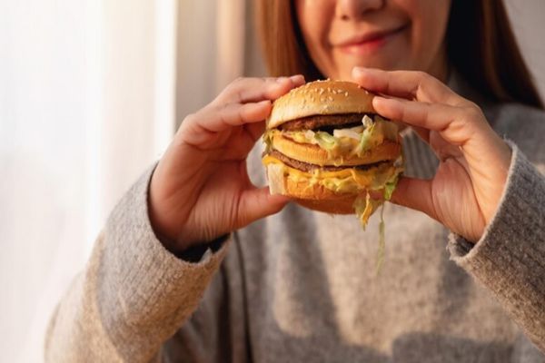 Acné - Mujer con un jersey de manga larga a punto de comerse una hamburguesa