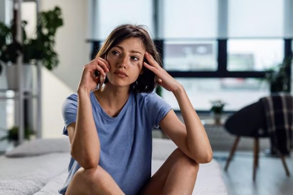 Hipertiroidismo - Mujer sentada en el colchón de su cama llamando por teléfono con signos claros en su cara de agotamiento y no dormir bien