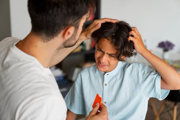 tiña del cuero cabelludo - padre revisando la cabeza de su hijo el cual se esta rascando la cabeza 