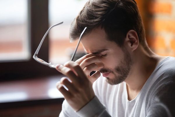 Hombre sentado en la mesa llevándose la mano a los ojos con signos de cansancio en la vista