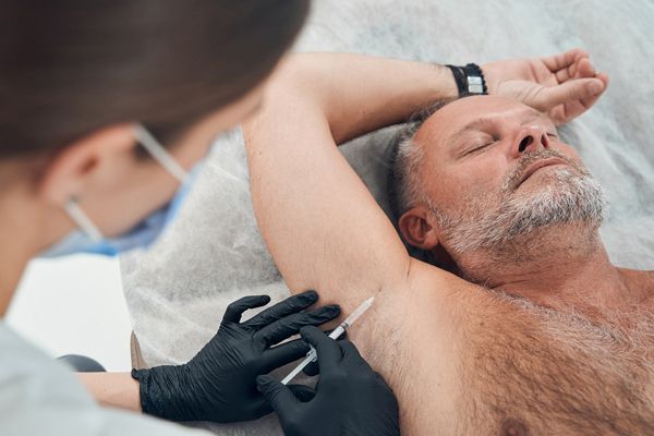 Hombre mayor en la consulta de la especialista inyectándose toxina botulínica para regular la sudoración