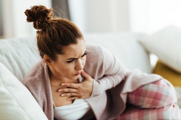 Mujer recostada en el sofá llevándose la mano al pecho con signos de tener nauseas