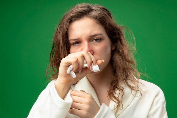Alergias - Mujer con un albornoz y un pañuelo en la mano con la nariz congestionada por culpa de una alergia