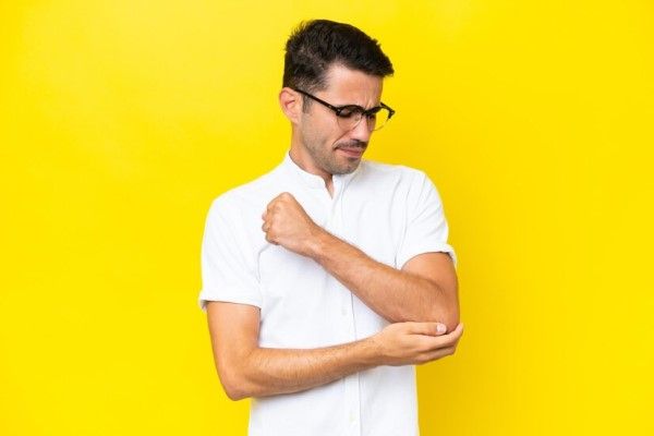 sarcoma - hombre blanco tocándose el codo por dolor en la zona, síntoma de poder estar sufriendo un sarcoma