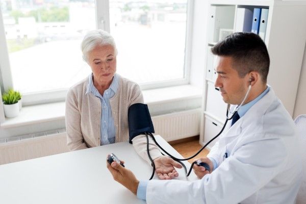 Hipotensión - mujer mayor tomándose la tensión en la consulta de su medico