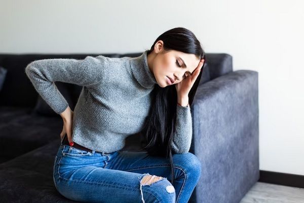 fibromialgia - mujer sentada en un sofá con fuertes dolores de espalda