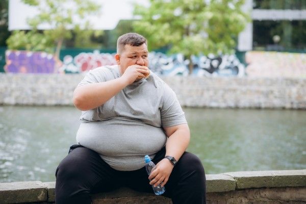 Un hombre muy gordo está comiendo una hamburguesa
