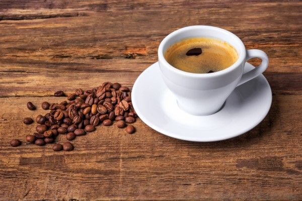 bruxismo - taza de cafe solo sobre mesa de madera con unos granos de café tostados