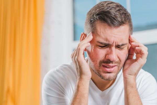 hombre blanco joven tocándose las sienes por el fuerte dolor de cabeza