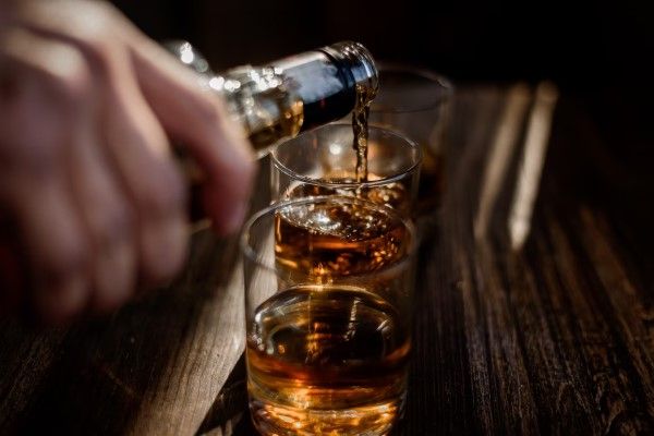 osteonecrosis - Verter bebidas alcohólicas fuertes en los vasos que están sobre la mesa de madera