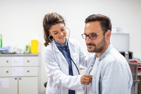 Joven doctora está usando un estetoscopio para escuchar los latidos del corazón del paciente