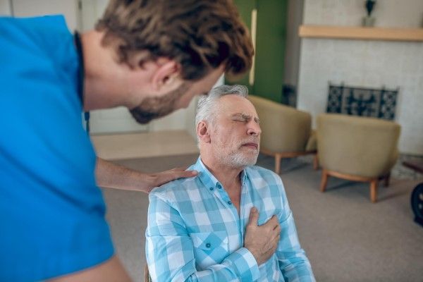 Doctor de pelo oscuro inclinándose hacia un hombre caucásico maduro con dolor en el pecho