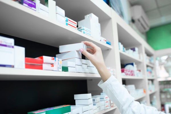 farmacéutica cogiendo una caja de medicamento de la estantería de la farmacia