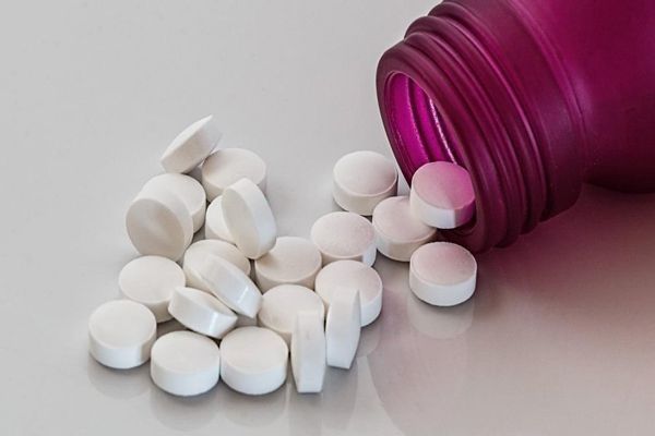 Imagen de un bote de medicamentos tumbado en la mesa y las pastillas saliendo del bote