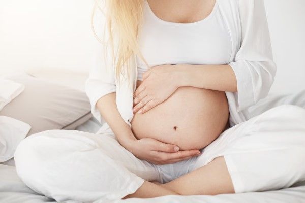 Joven embarazada que pronto será madre tocando su vientre sentado en su dormitorio por la tarde