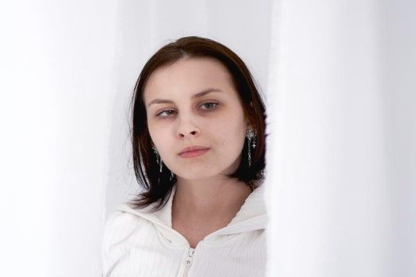 estrabismo - mujer blanca con estrabismo en su cuarto entre las cortinas