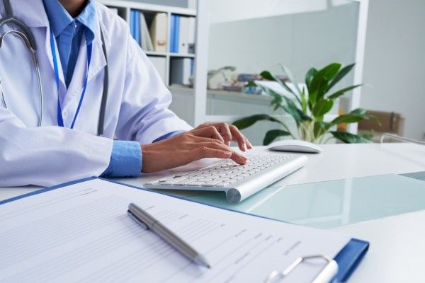  Manos de doctora irreconocible escribiendo en el teclado en la oficina