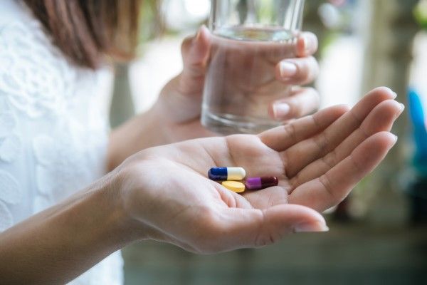 mujer con un vaso de agua en una mano y pastillas en la otra