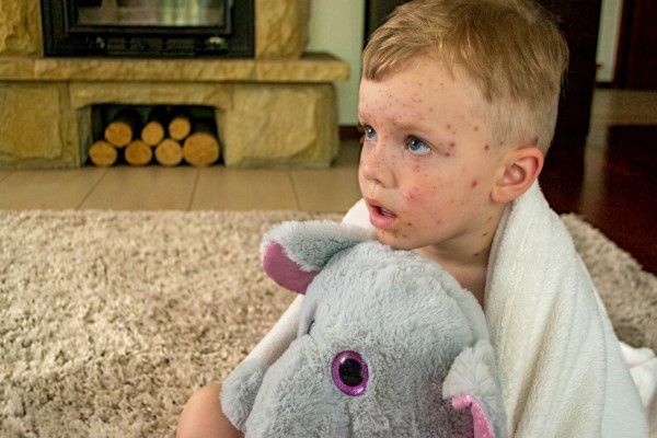 niño blanco enfermo agarrado a su peluche de elefante cubierto con una manta sobre la alfombra del salón