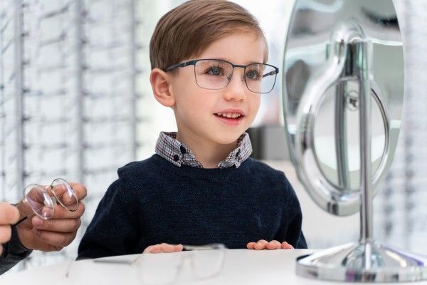 niño con jersey azul y camisa a cuadros en el oculista probándose gafas