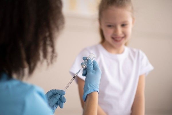  Joven médico de espaldas vacunando a una niña blanca sonriente