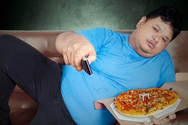 hombre obeso tumbado en el sofá con una pizza