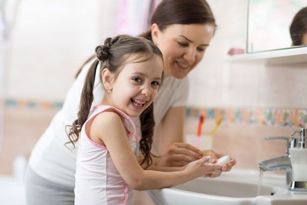 Niña sonriente practica el eficiente lavado de manos junto a su madre
