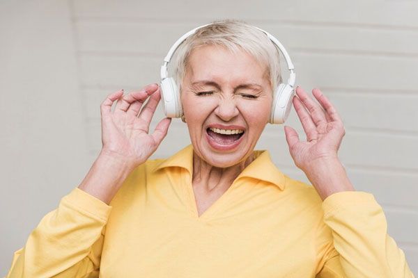 Pérdida de la audición - Mujer de cabello canoso escucha música con audífonos a todo volumen 
