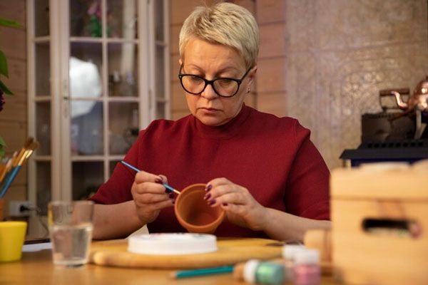 Enfermedad de Alzheimer - Mujer de lentes con cabello corto decora unas macetas de barro para desplegar sus habilidades artísticas