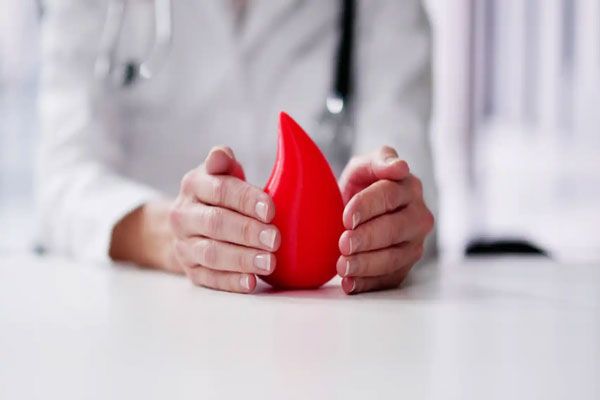 Hemofilia - Doctora encierra una gran gota de sangre con sus manos como símbolo de consciencia y cuidado ante el sangrado excesivo 