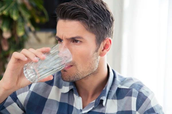 Hepatitis A - Hombre con camisa de cuadros tomando un vaso de agua del grifo 