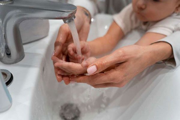 Madre enseña a un niño pequeño como debe llevar a cabo un correcto lavado de manos en casa