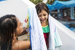 Madre seca el cabello de su hija tras salir de la piscina para evitar que le entre agua en el oído