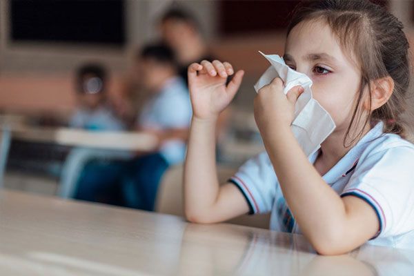 Escarlatina - Niña sacude enérgicamente su nariz con un pañuelo mientras se encuentra en el colegio 