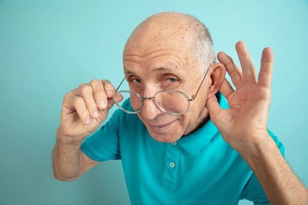 Pérdida de la audición - Adulto mayor con gafas y de camisa azul para la oreja para escuchar mejor 