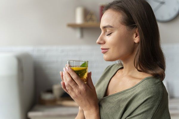 Mujer se sienta en el sofá con los ojos cerrados para tomarse una infusión de hierbas relajadamente