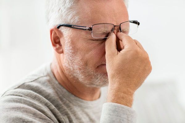 Glaucoma - Adulto mayor con lentes se sujeta la nariz ante persistentes molestias en la vista