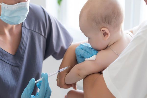 Meningitis bacteriana - Enfermera con tapaboca pincha el brazo de un bebé para inmunizarlo contra diversas enfermedades