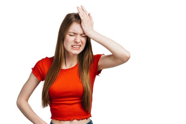 herpes labial u oral - mujer joven llevándose la mano a la cabeza con gesto de dolor