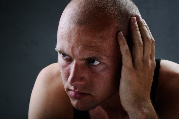 hombre joven rapado con la mano en el lateral de la cabeza y cara muy seria