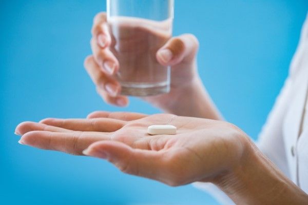 mujer con una pastilla en una mano y un vaso de agua en la otra