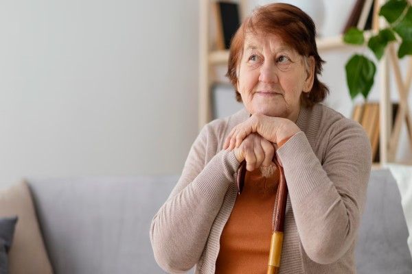 Colitis isquémica - mujer mayor sentada en el sofá apoyando la cabeza en las manos que sujetan un bastón