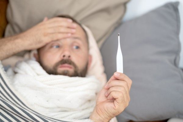 Fiebres de origen desconocido - Hombre enfermo acostado en el sofá comprobando su temperatura en casa en la sala de estar