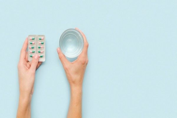 Colitis isquémica - mujer con un blíster de píldoras en una mano y un vaso de agua en la otra