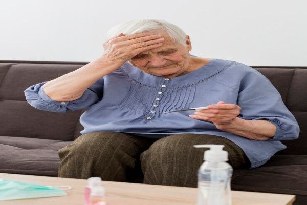 Flebitis - mujer mayor sentada en el sofá con la mano en la cabeza mirando un termómetro