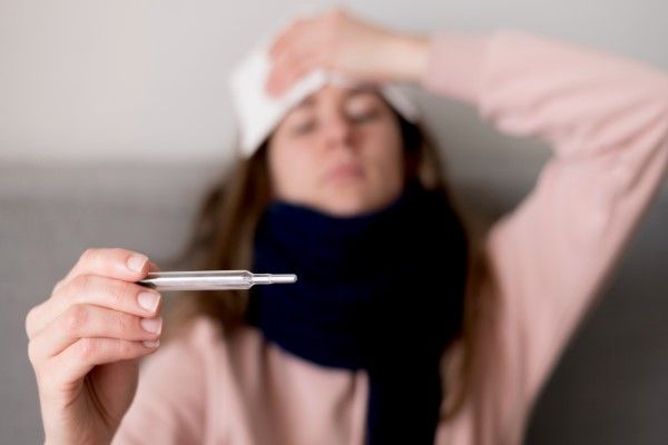 mujer en el sofá comprobando si tiene fiebre en el termómetro